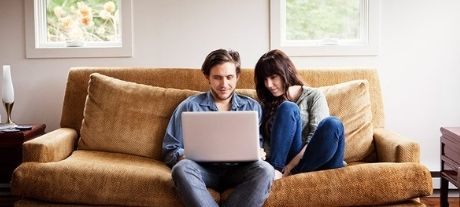 Young couple sat on sofa looking at a laptop