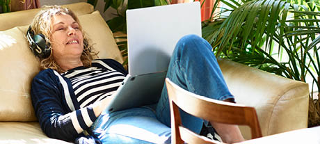 Woman laid on sofa with headphones and laptop
