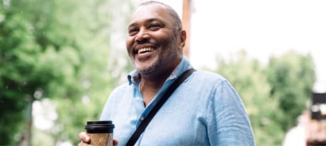 Smiling man outside wearing a shirt and over shoulder bag with travel cup of coffee