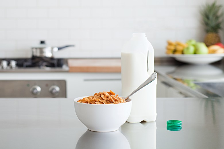 Bowl of cornflakes on kitchen table next to bottle of semi-skimmed milk