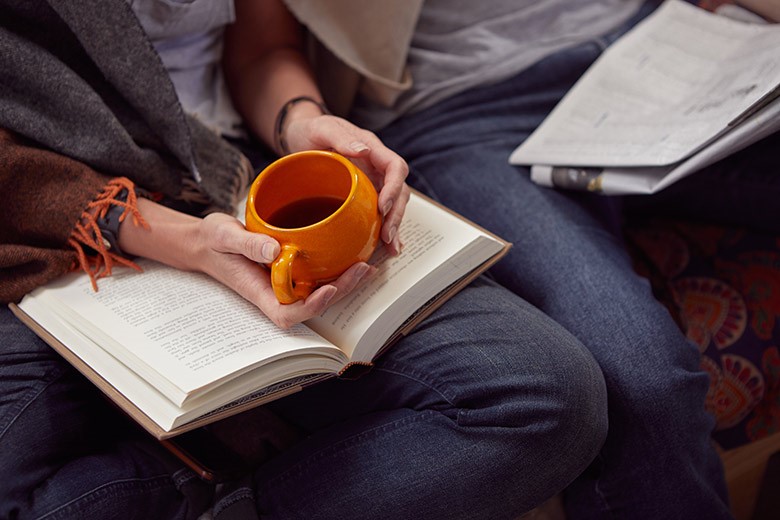 Couple sat on sofa reading and drinking coffee