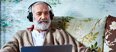 Man sat in front of a laptop with headphones on looking into the distance