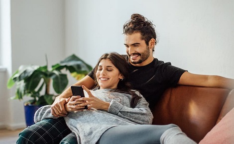 Couple sat of sofa smiling at a phone