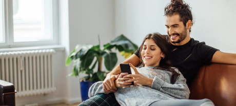 Couple sat on a sofa smiling at a phone