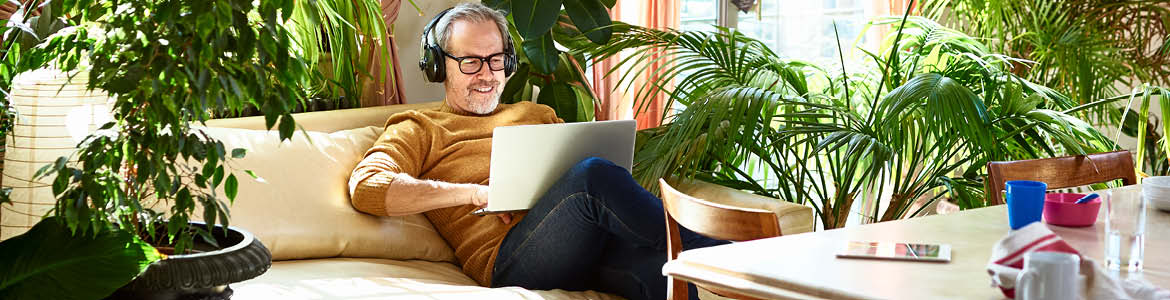 Man with headphones on, looking at a laptop and smiling.