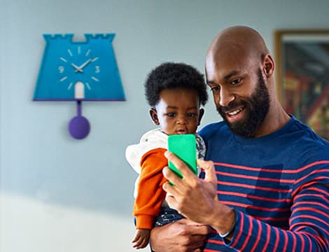 Father holding toddler son showing him his phone