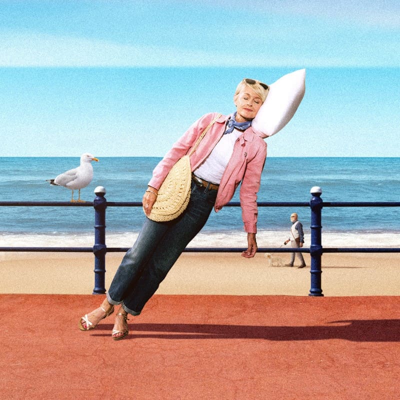 A relaxed woman leaning mid-air on a pillow with a beach background.