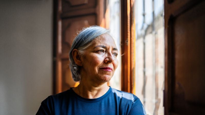 Woman in blue shirt looking outside of window.