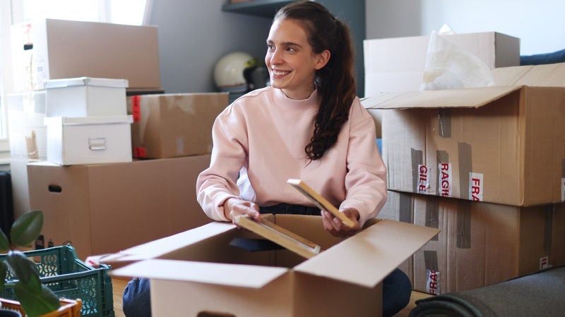 Woman surrounded by packing boxes smiles while taking out picture frames out of box.