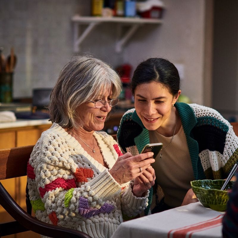 Older woman showing smiling young woman something on her phone.
