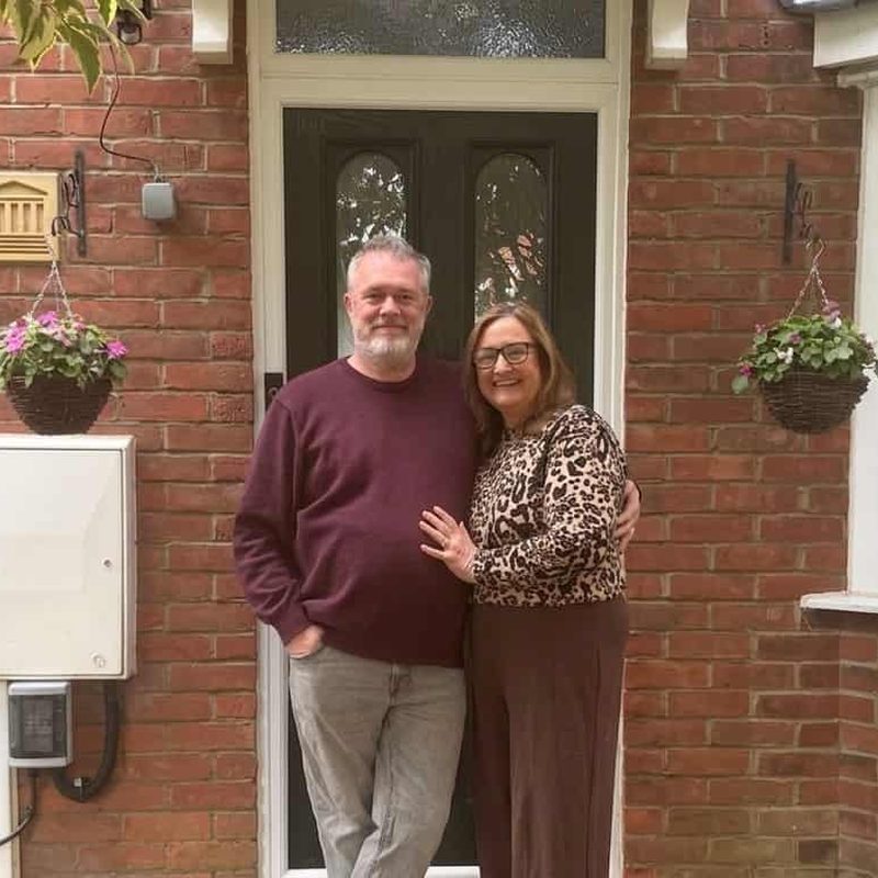 Couple standing smiling in front of house.
