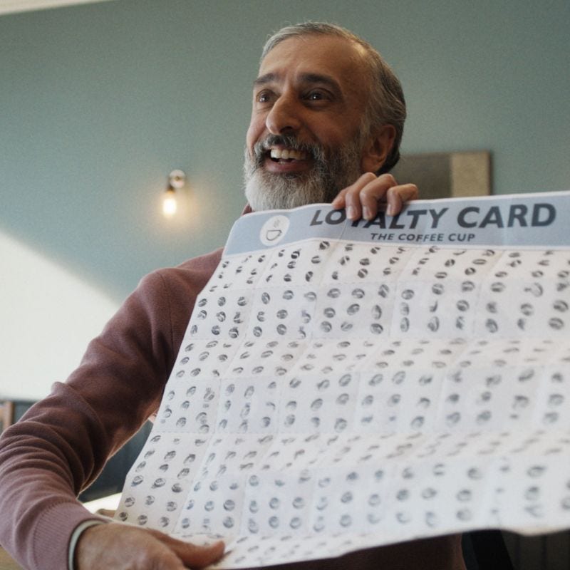Smiling man with a grey beard holding up a large loyalty card