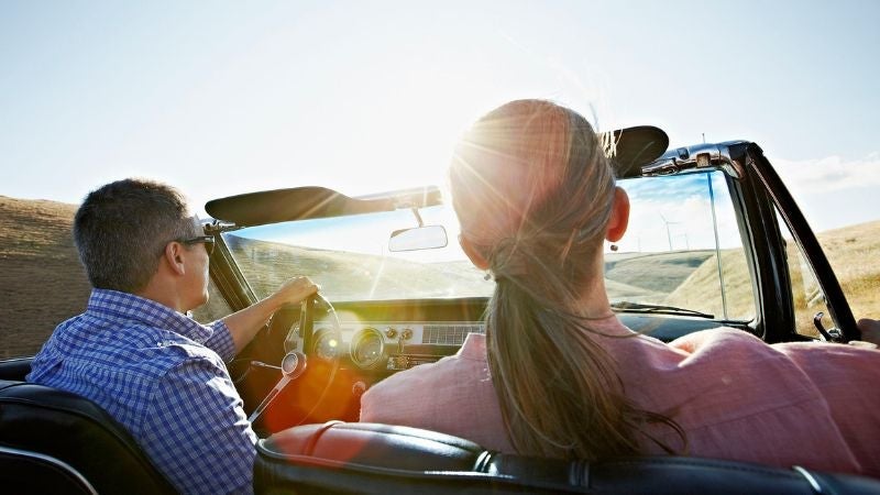 A backseat view of a man and woman's heads in a car, with bright sunshine coming through the windshield.