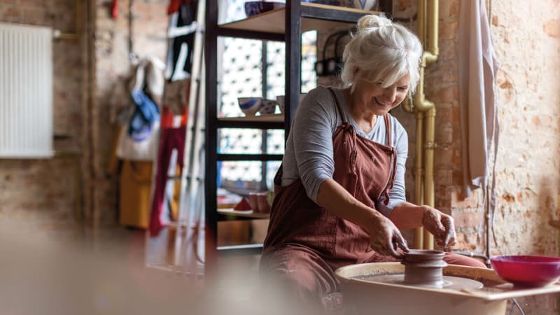 Woman turning a clay pot on a pottery wheel in a pottery studio.