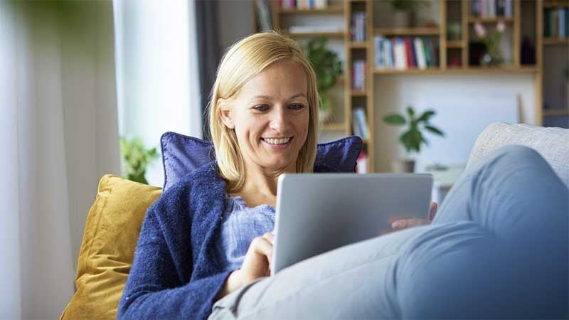 Woman sat on sofa smiling at tablet