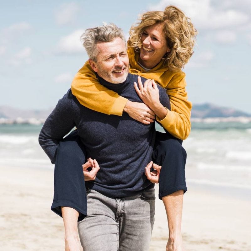 A man carrying a woman on his back, walking down the beach